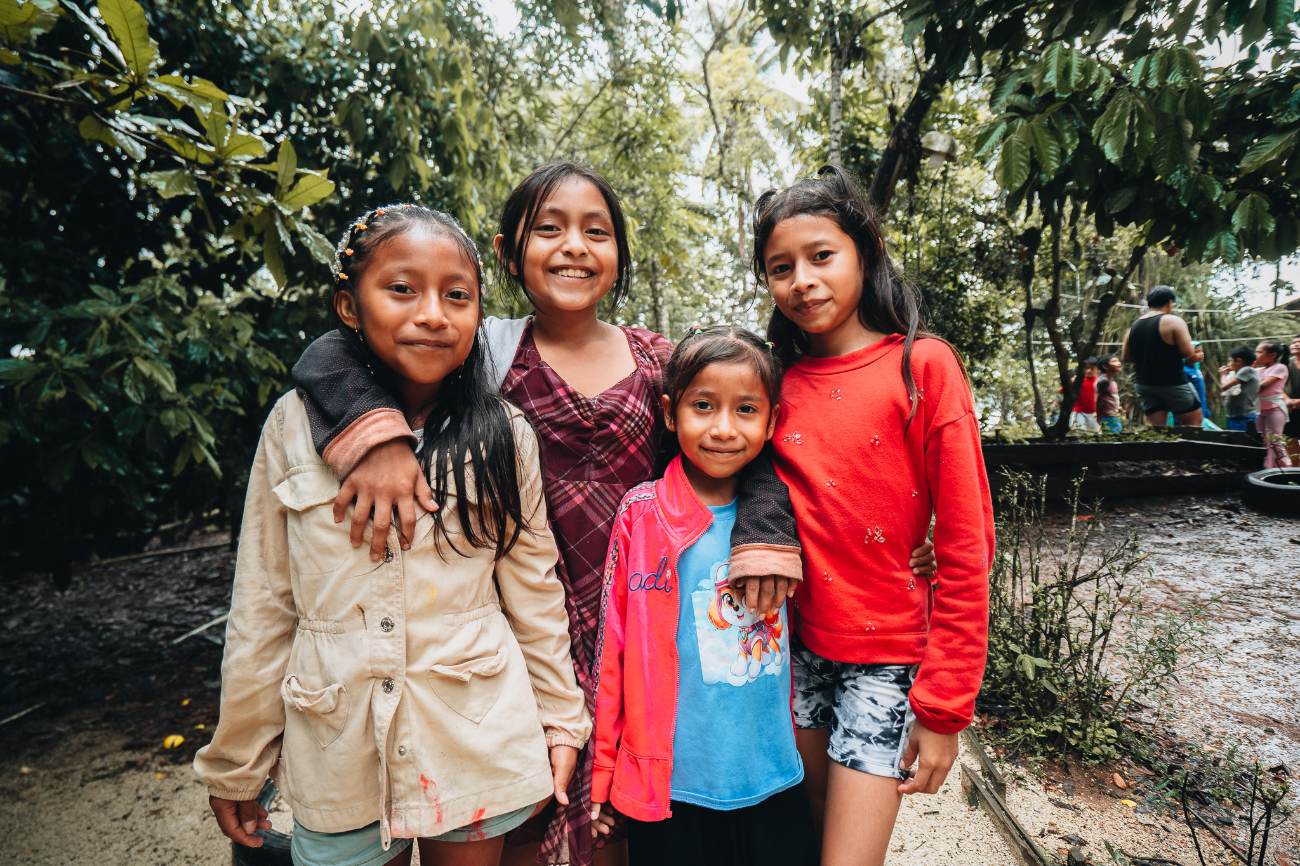Four young girls standing arm in arm and smiling under tropical trees