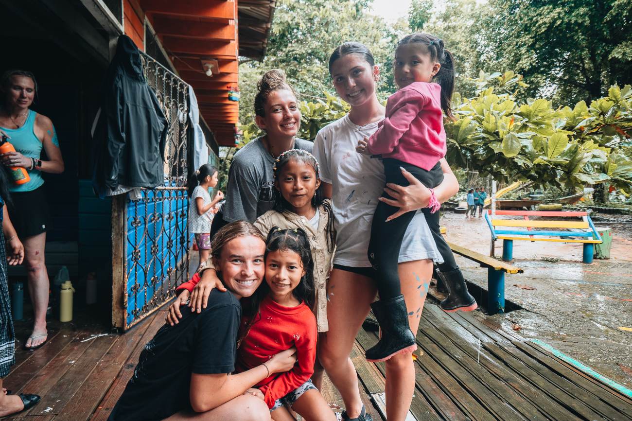 Students and young girls smiling together on a wooden porch after rain