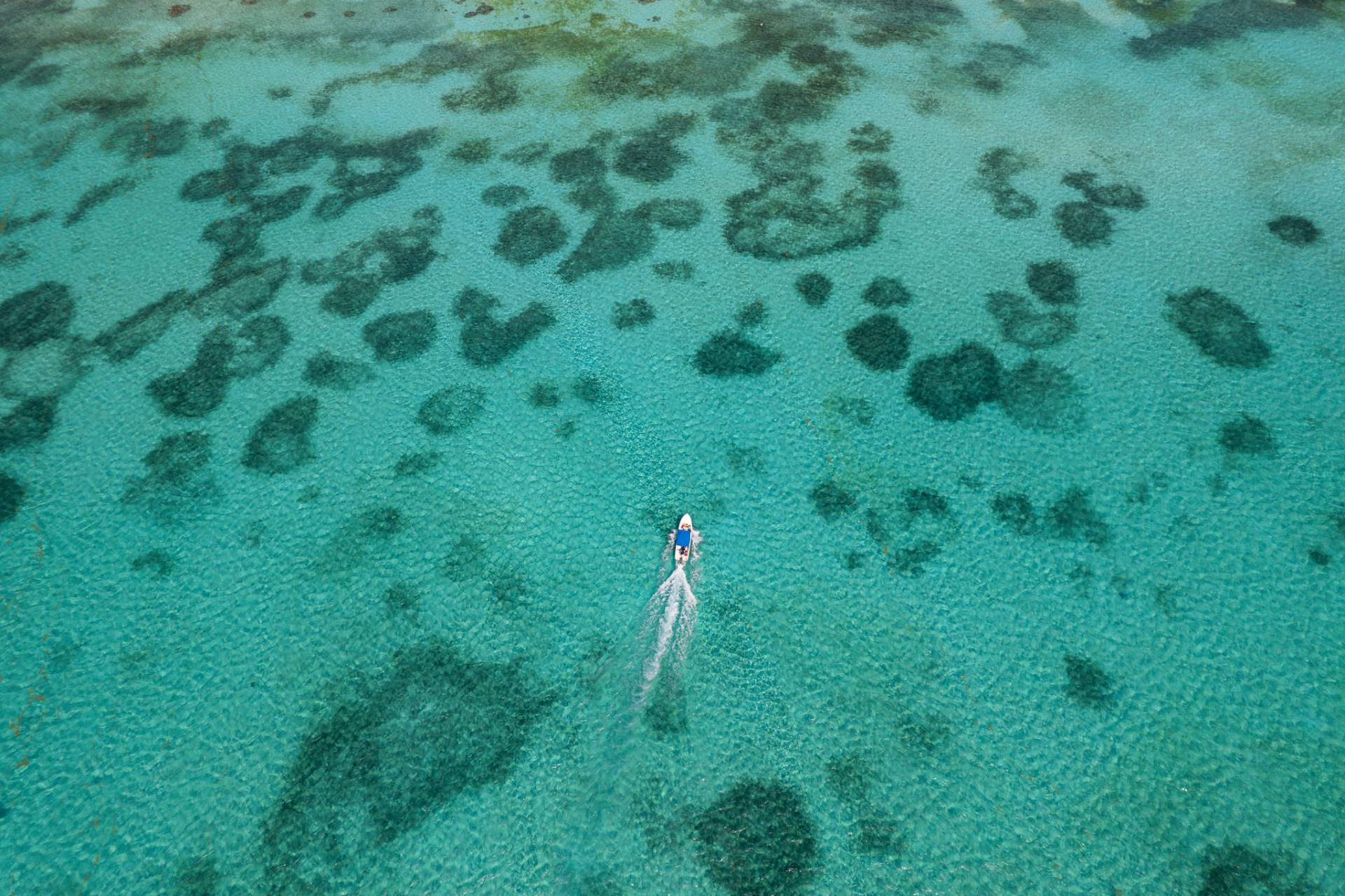 Aerial view of a small boat crossing clear shallow water over patch reefs