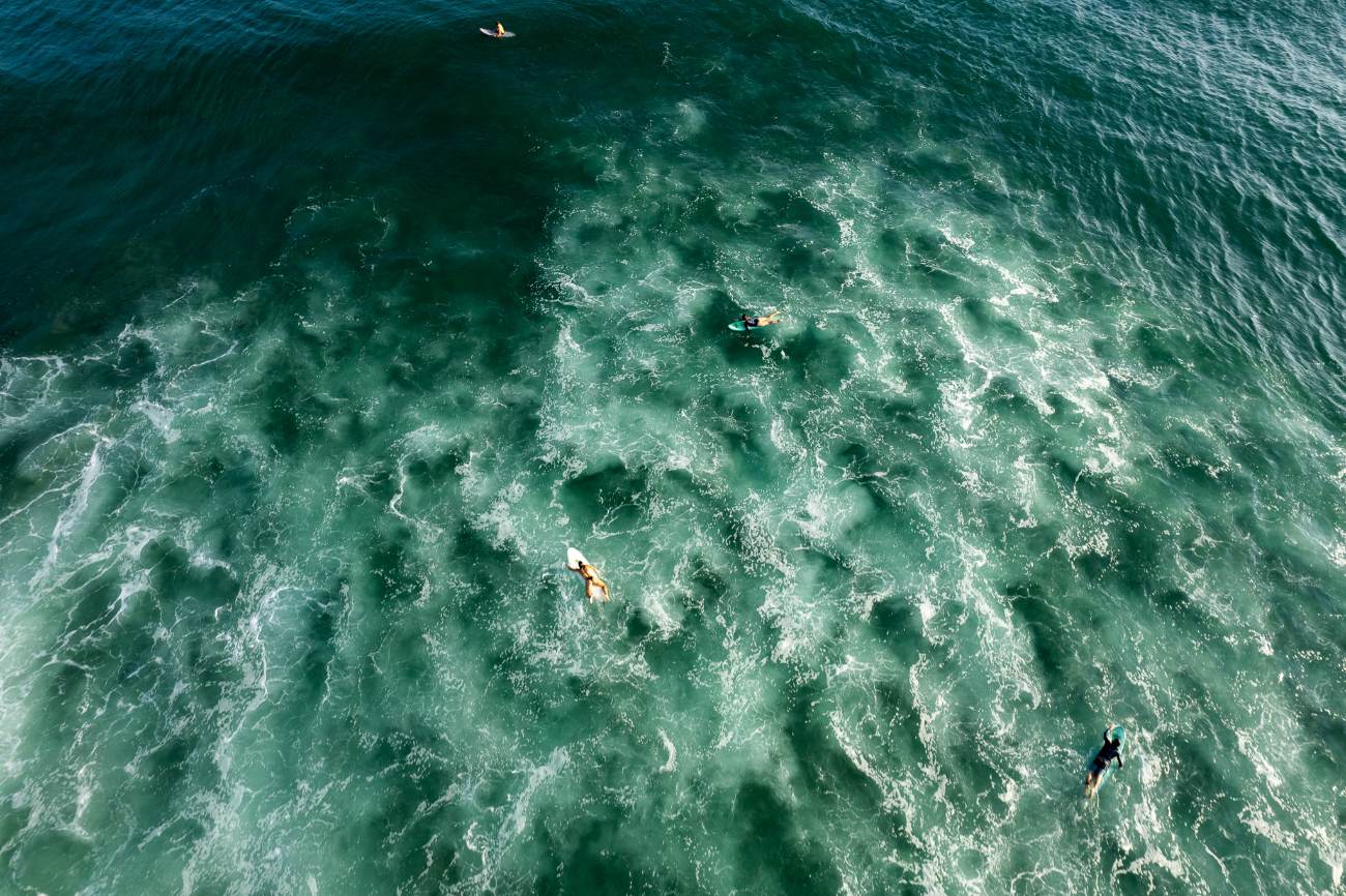 Aerial view of surfers paddling through white water over a green sea
