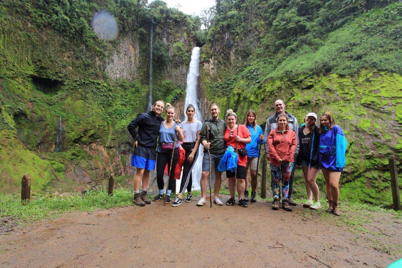 A student group standing together in front of a tall highland waterfall