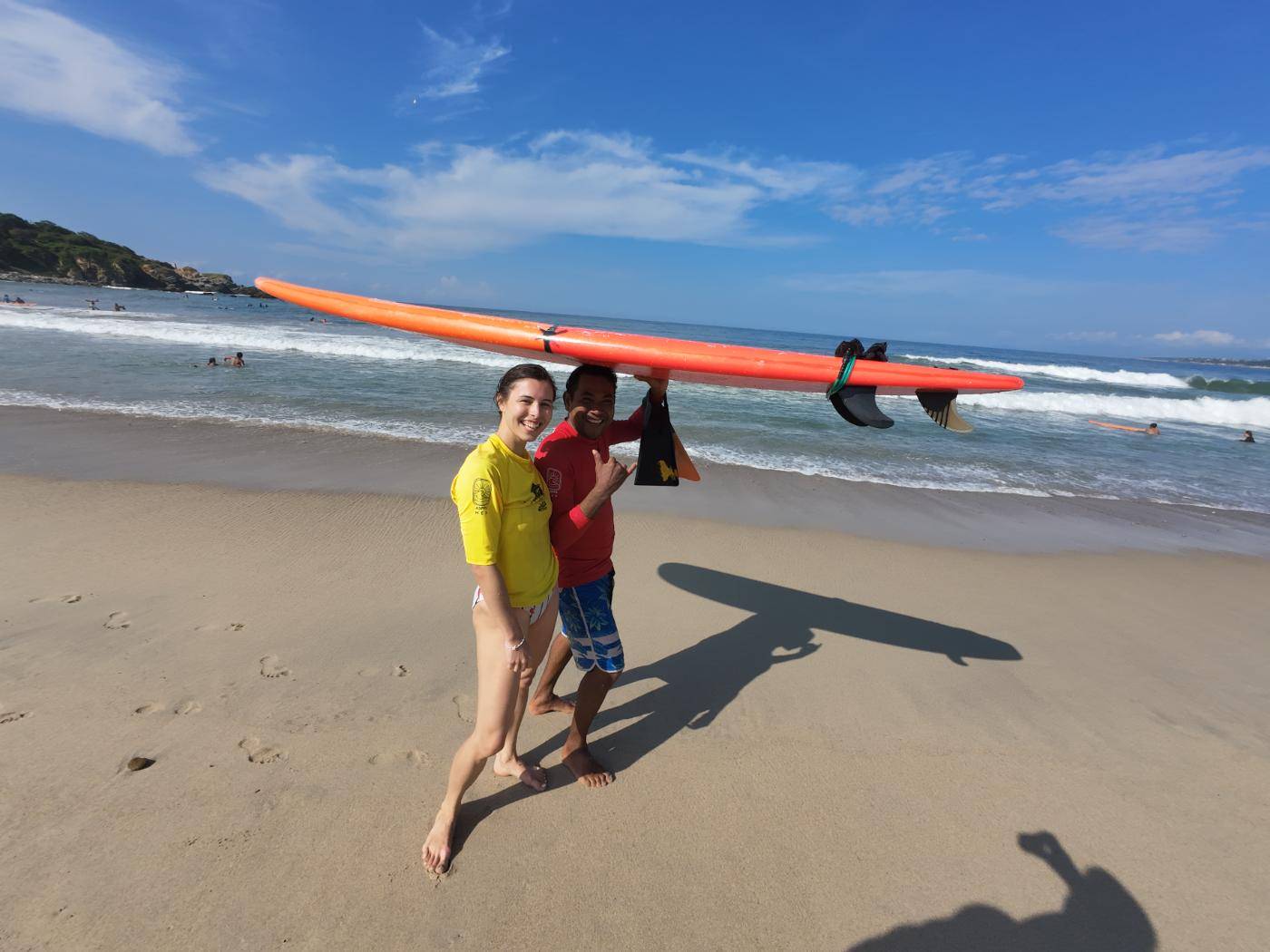 Two students carrying a surfboard across the beach toward the water