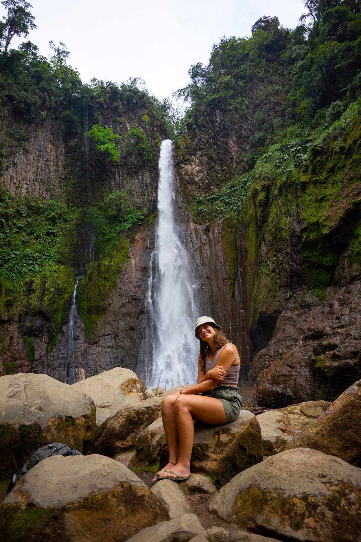 A hiker resting on the rocks beneath a narrow waterfall